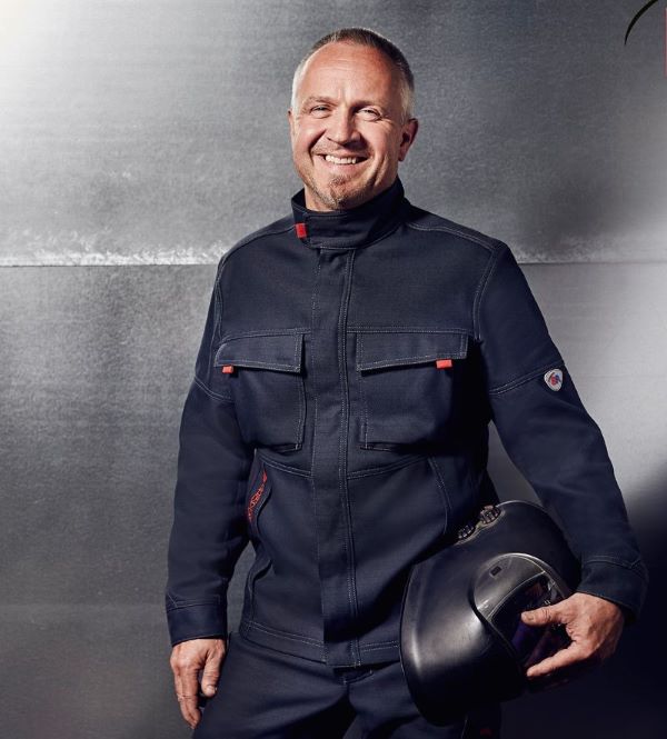 Ein Mann trägt eine dunkle Schweisserschutzjacke und hält einen Schutzhelm in der Hand.